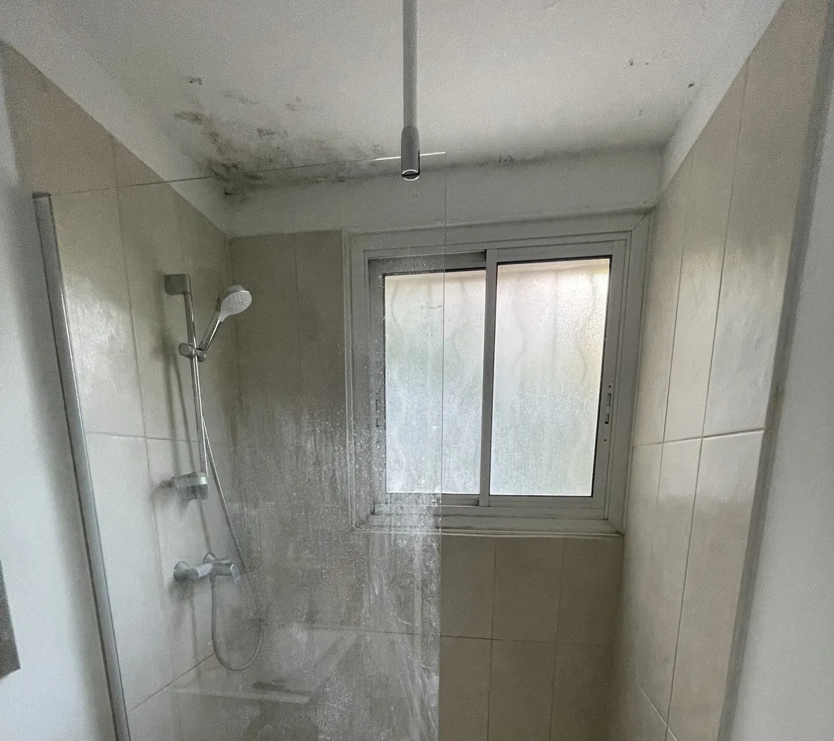 Moisissures noires à la jonction du plafond et des murs d'une salle d'eau à Montpellier, au-dessus de la douche et de la fenêtre