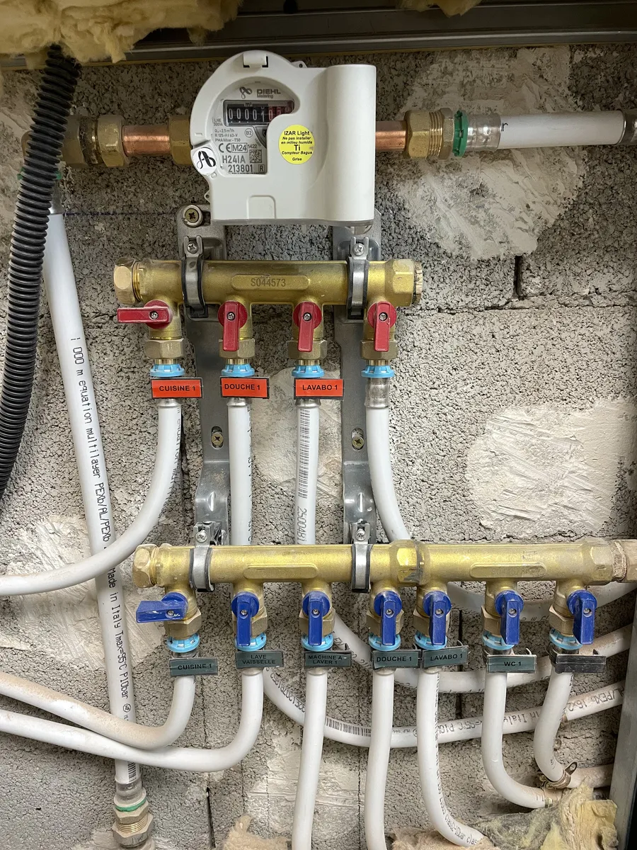 Nourrices de distribution en laiton dans un logement à Montpellier : départs en PER sous fourreau, vannes rouges pour l'eau chaude, bleues pour l'eau froide, chaque départ étiqueté par poste